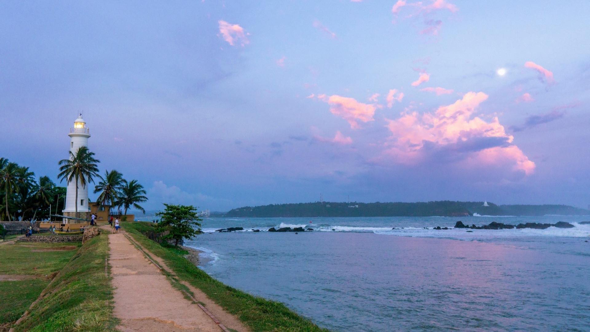 Sunset over the grassy ramparts at Galle Fort on Sri Lanka's south coast, with the white lighthouse tower against pink cloud
