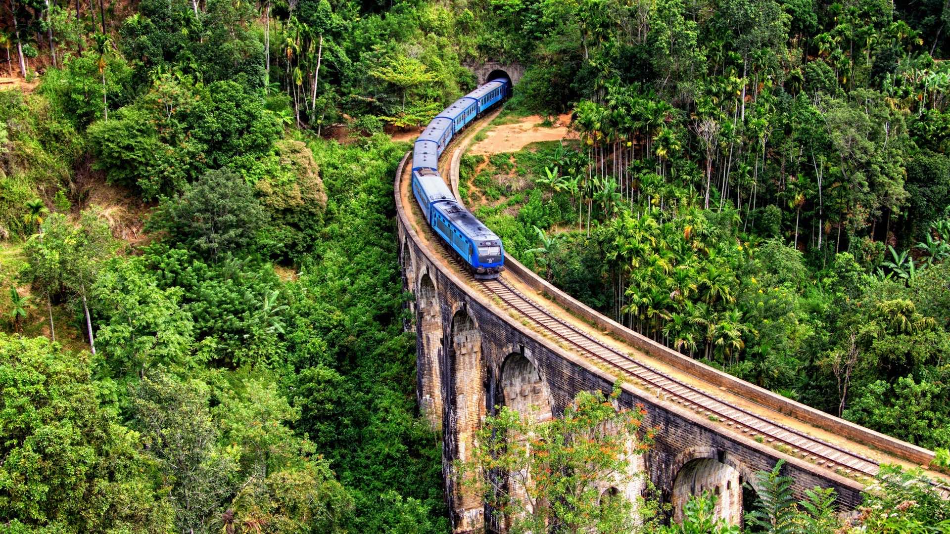 A blue Sri Lankan train crossing the stone Nine Arch Bridge above dense jungle at Ella